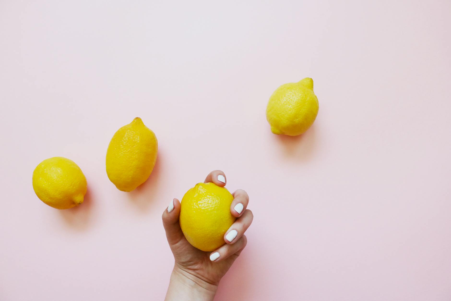 A hand holding a bright lemon on a soft pink background, symbolizing refreshing pleasure and sensation